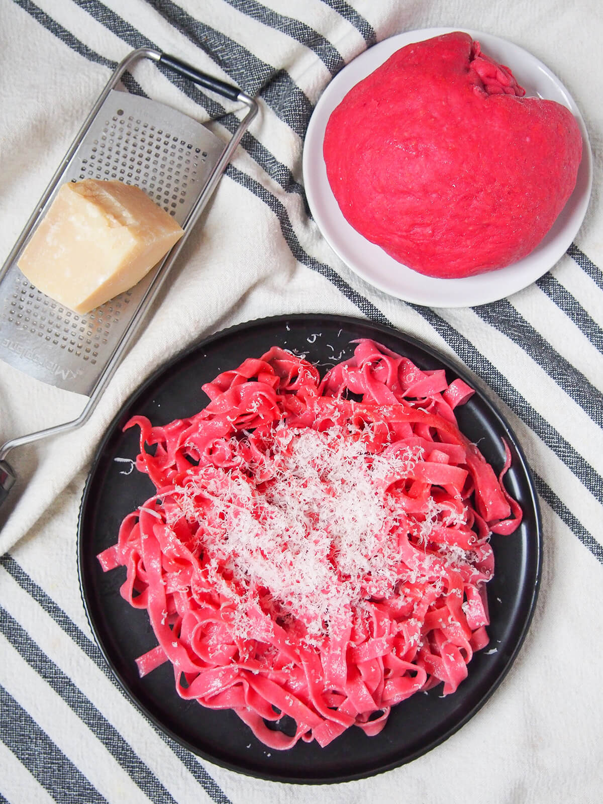 overhead view of plate of beet pasta with parmesan on top and ball of beet pasta dough.