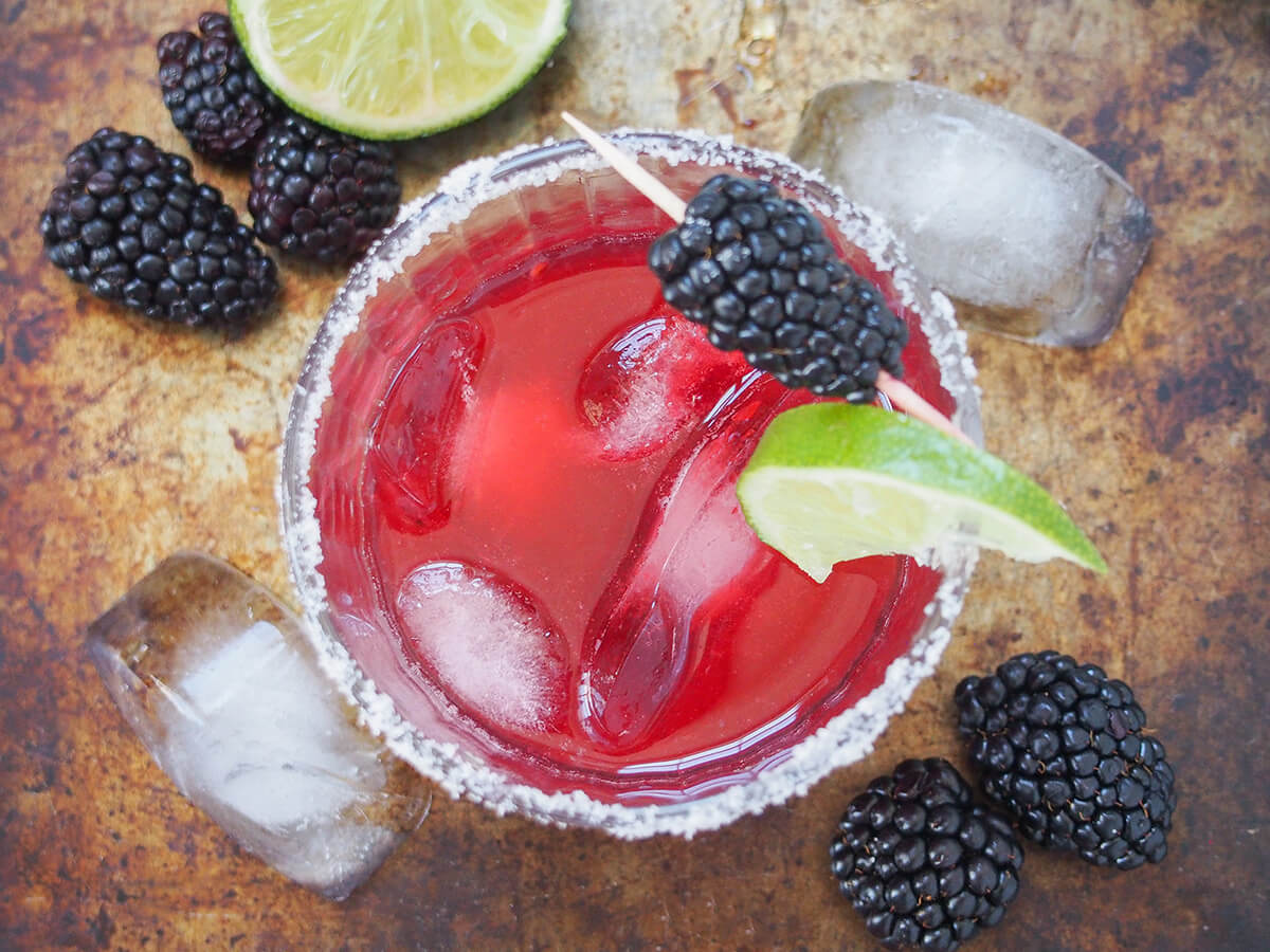 overhead view of a glass of blackberry margarita with blackberries and ice cubes around glass.