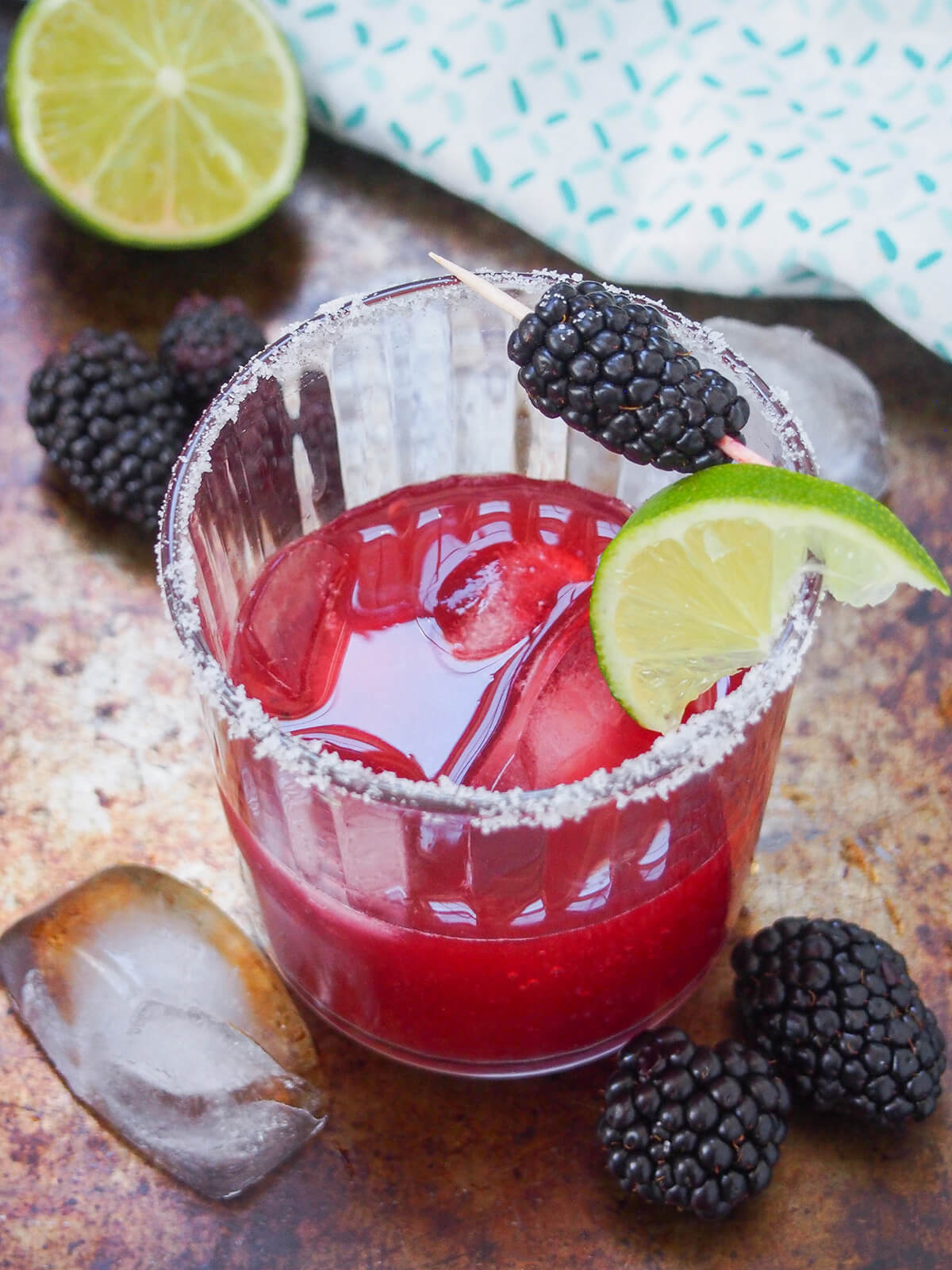 glass of blackberry margarita with blackberries and ice beside glass and cut lime behind.