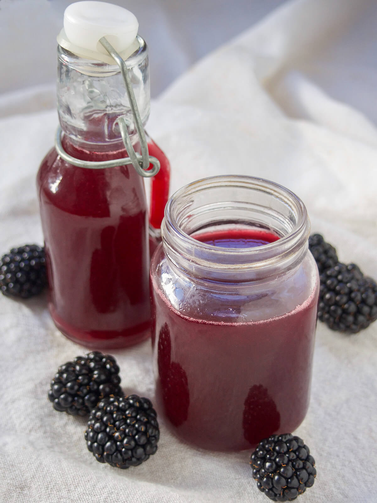 blackberry simple syrup in both a jar and a bottle with berries around them.