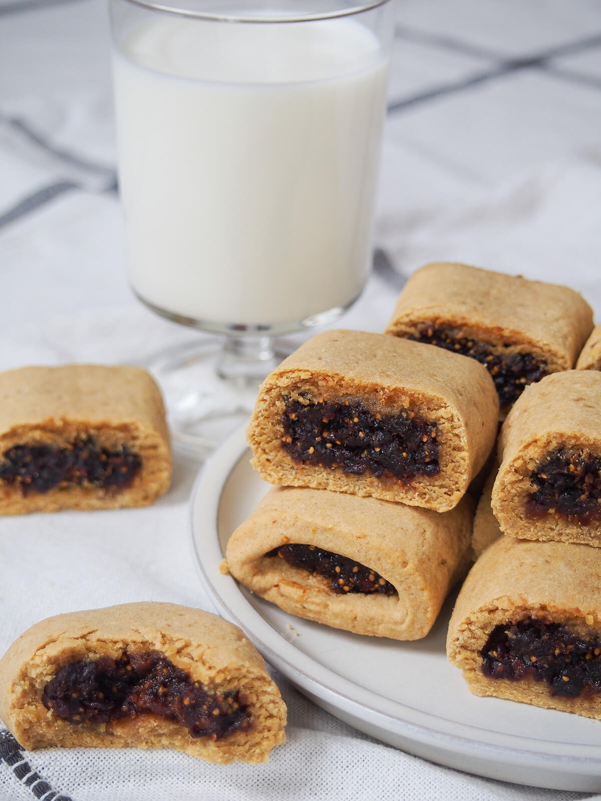 homemade fig Newtons on a plate with one bitten to side and glass of milk behind.