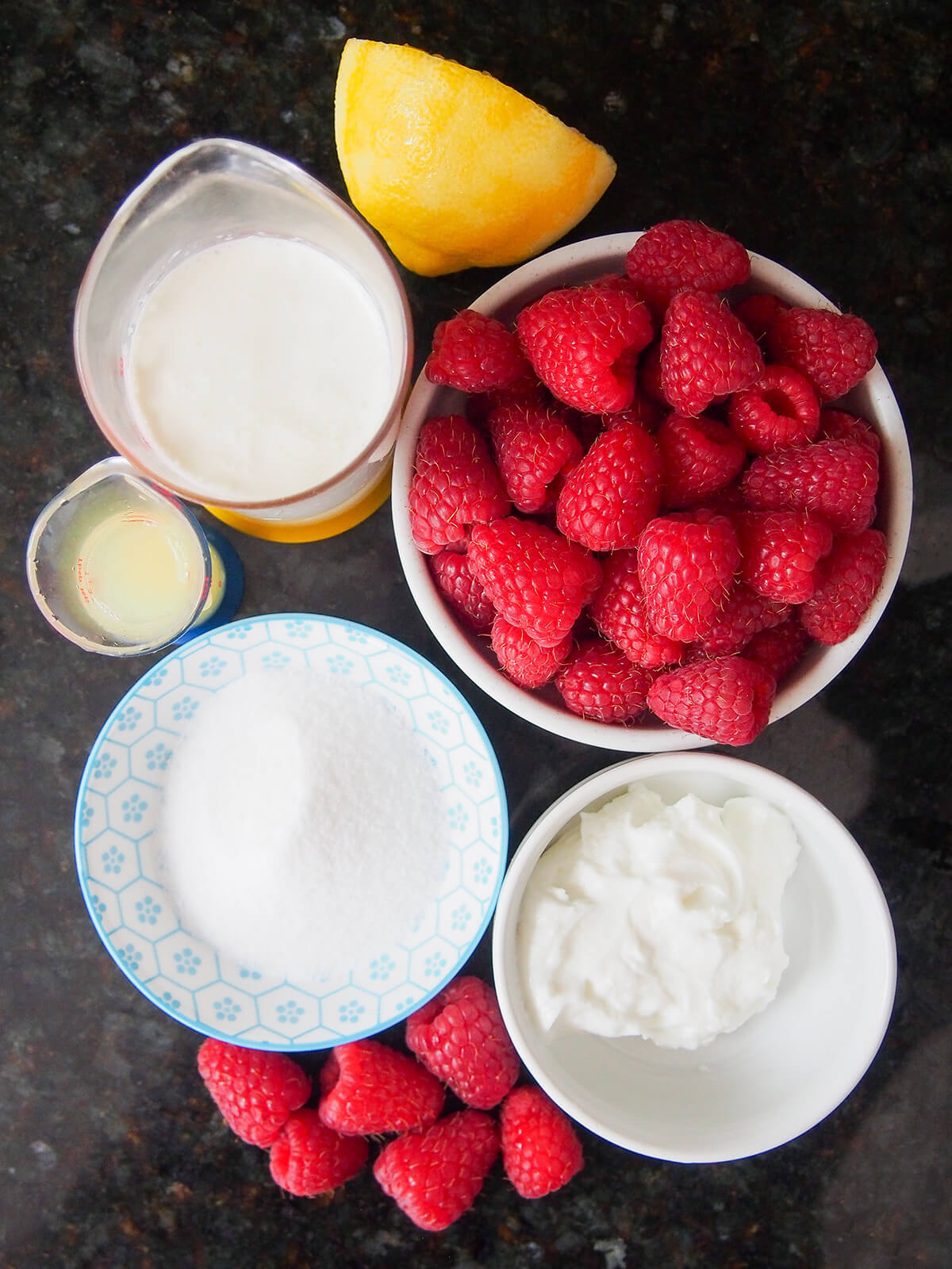 bowls of raspberries, yogurt, sugar and measures with cream and lemon juice.