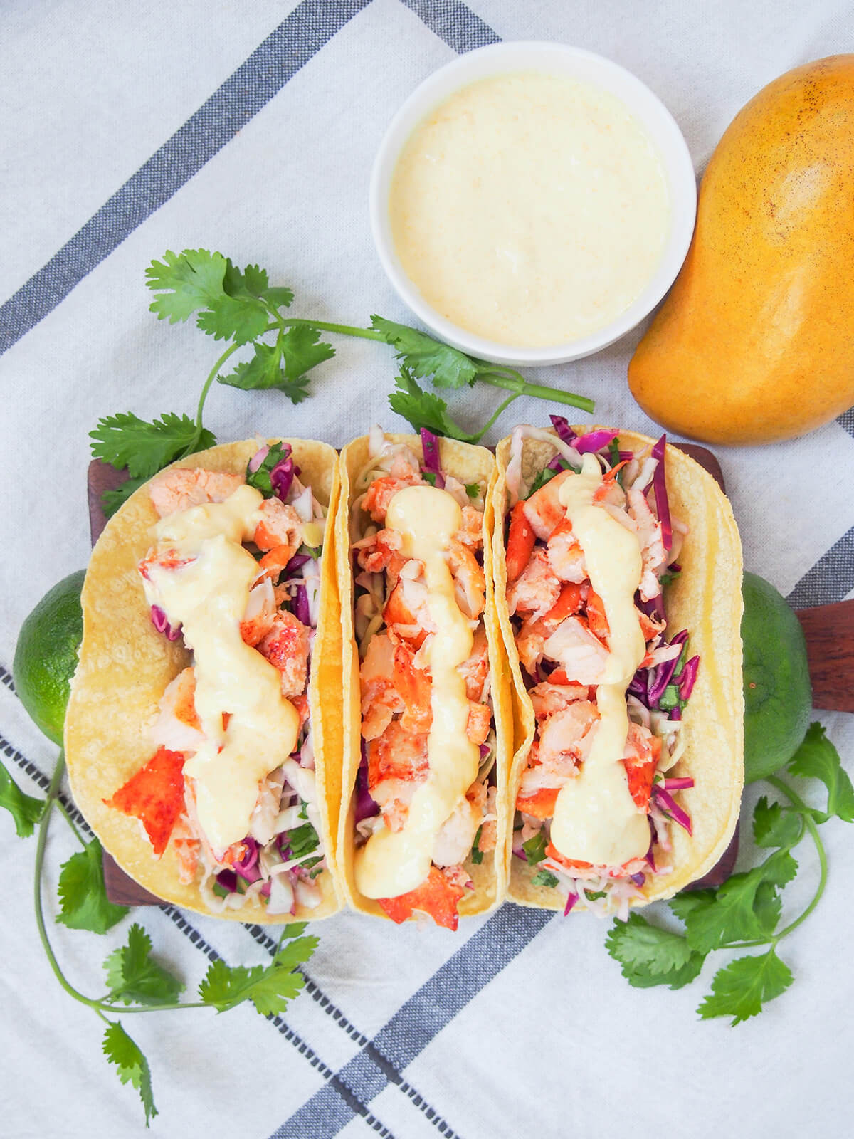 three lobster tacos from overhead with crema and mango above board.