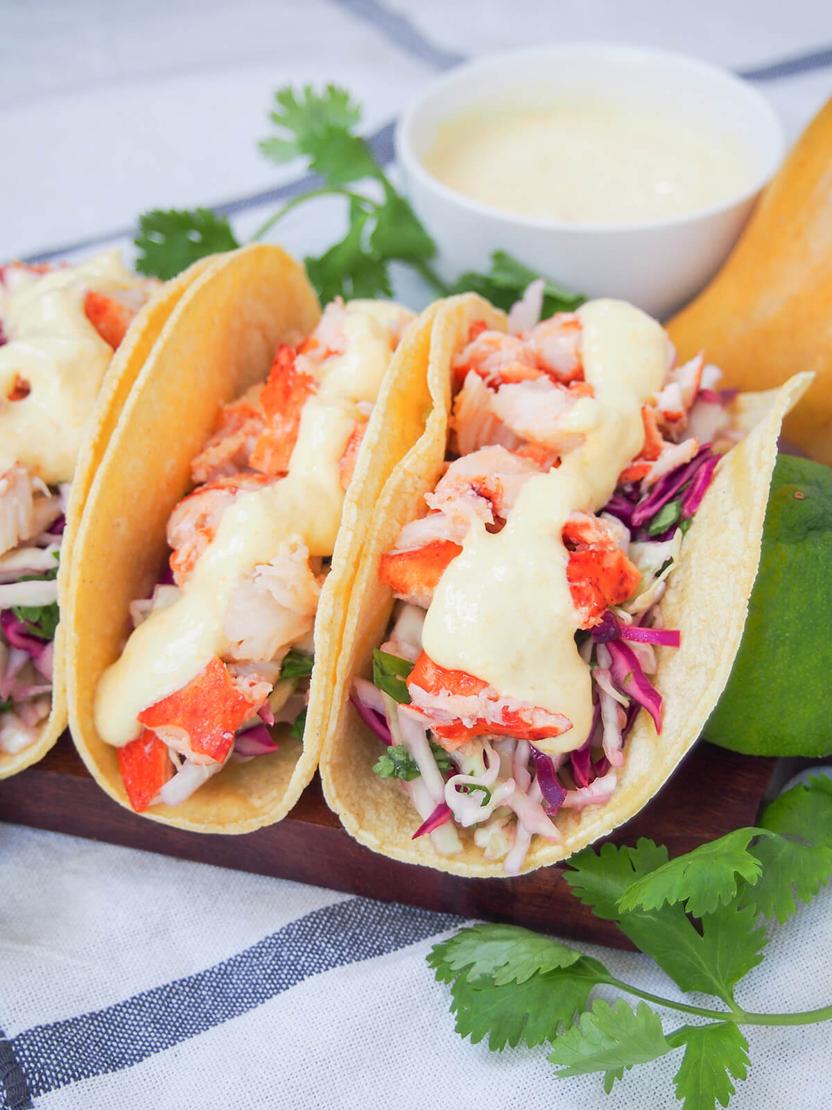 side view of lobster tacos with bowl with extra crema behind.