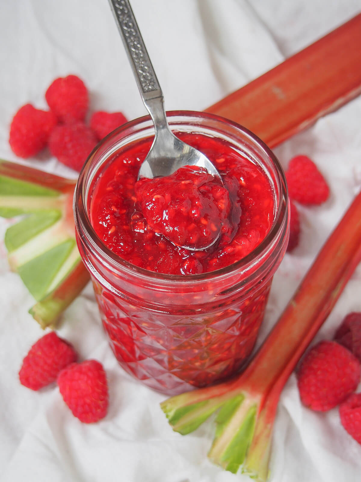jar of raspberry rhubarb jam with spoon of jam resting on top.