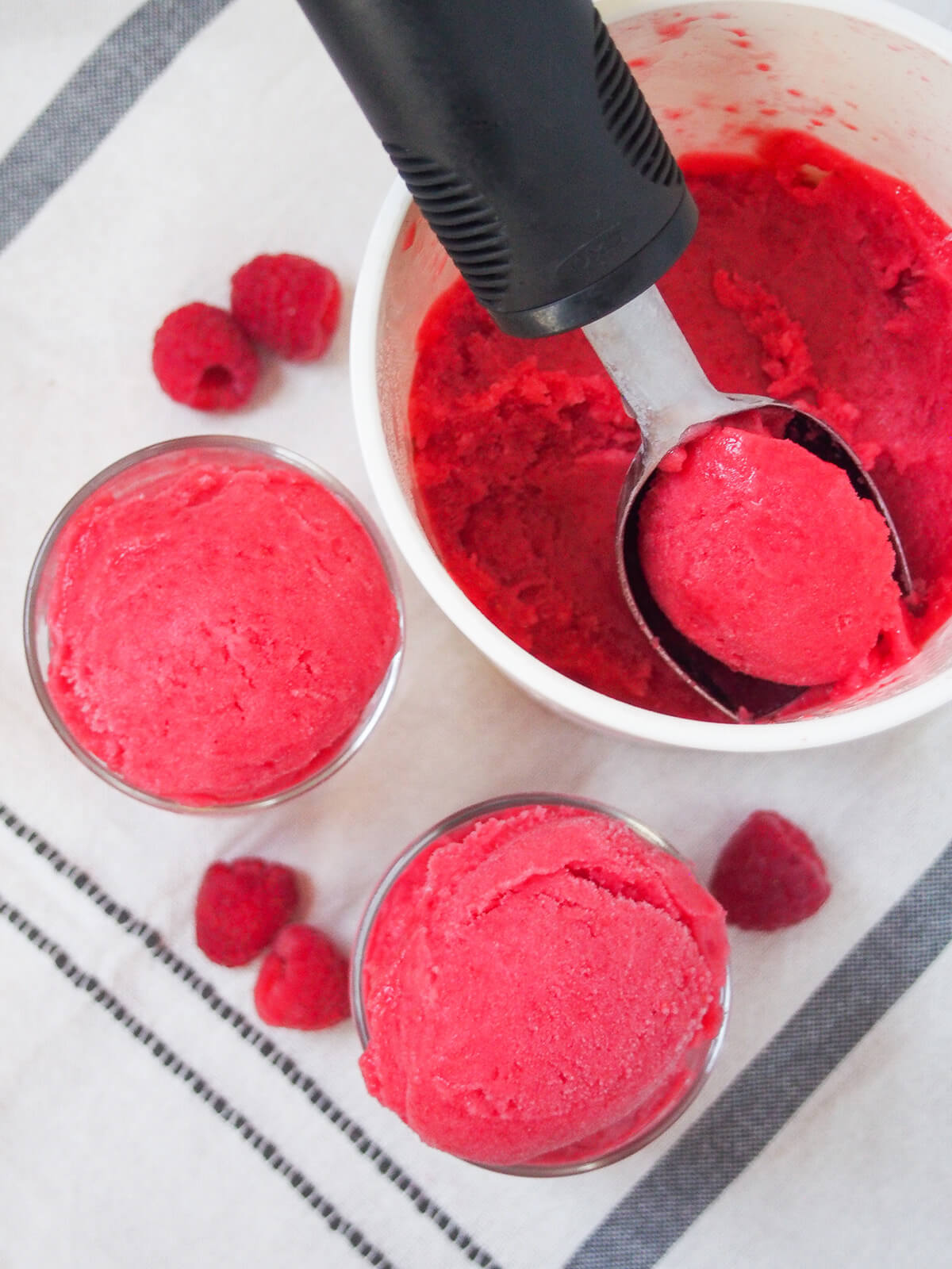overhead view of glasses with raspberry sorbet and scoop in tub.