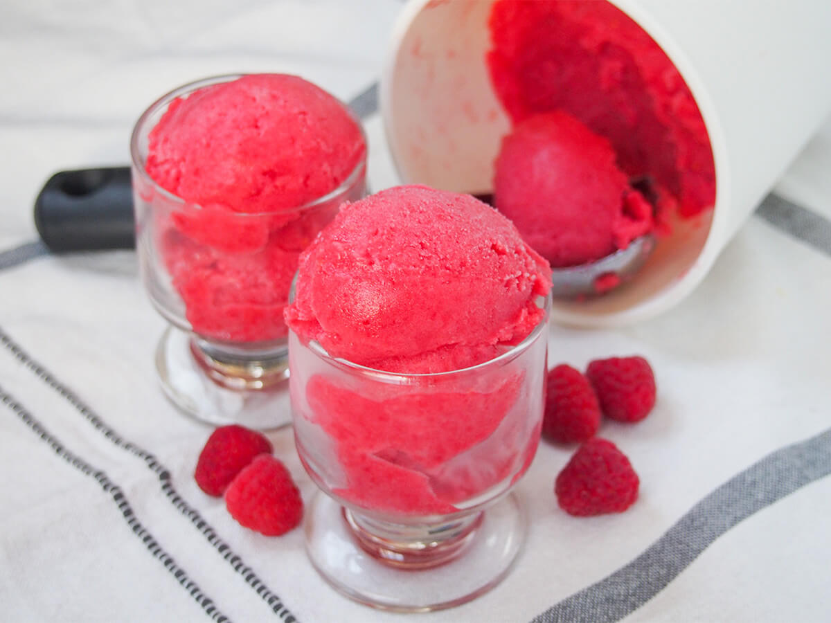 two small glasses filled with raspberry sorbet with scoop in tub on it's side behind.