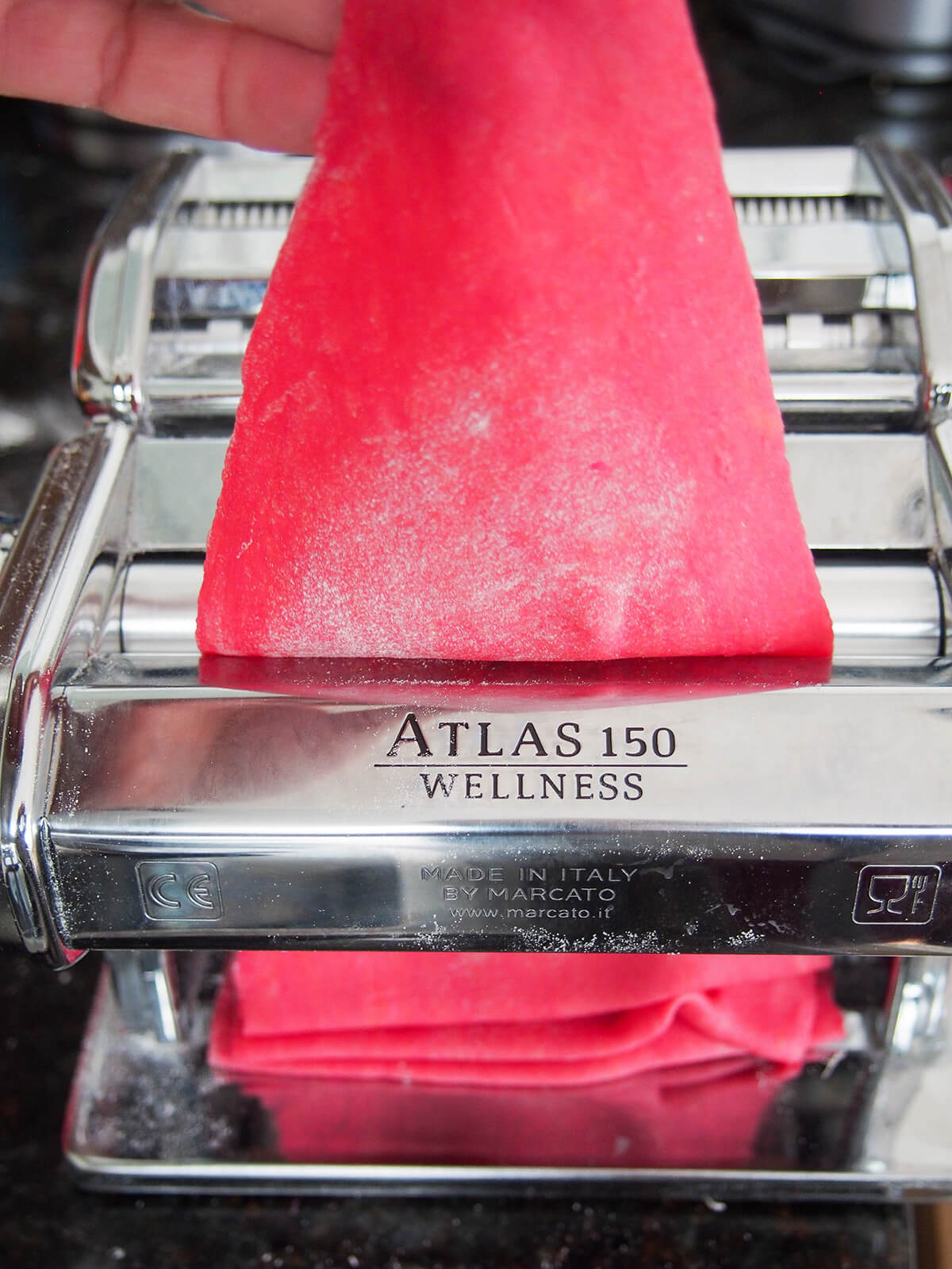 rolling a sheet of beet pasta dough through pasta machine.