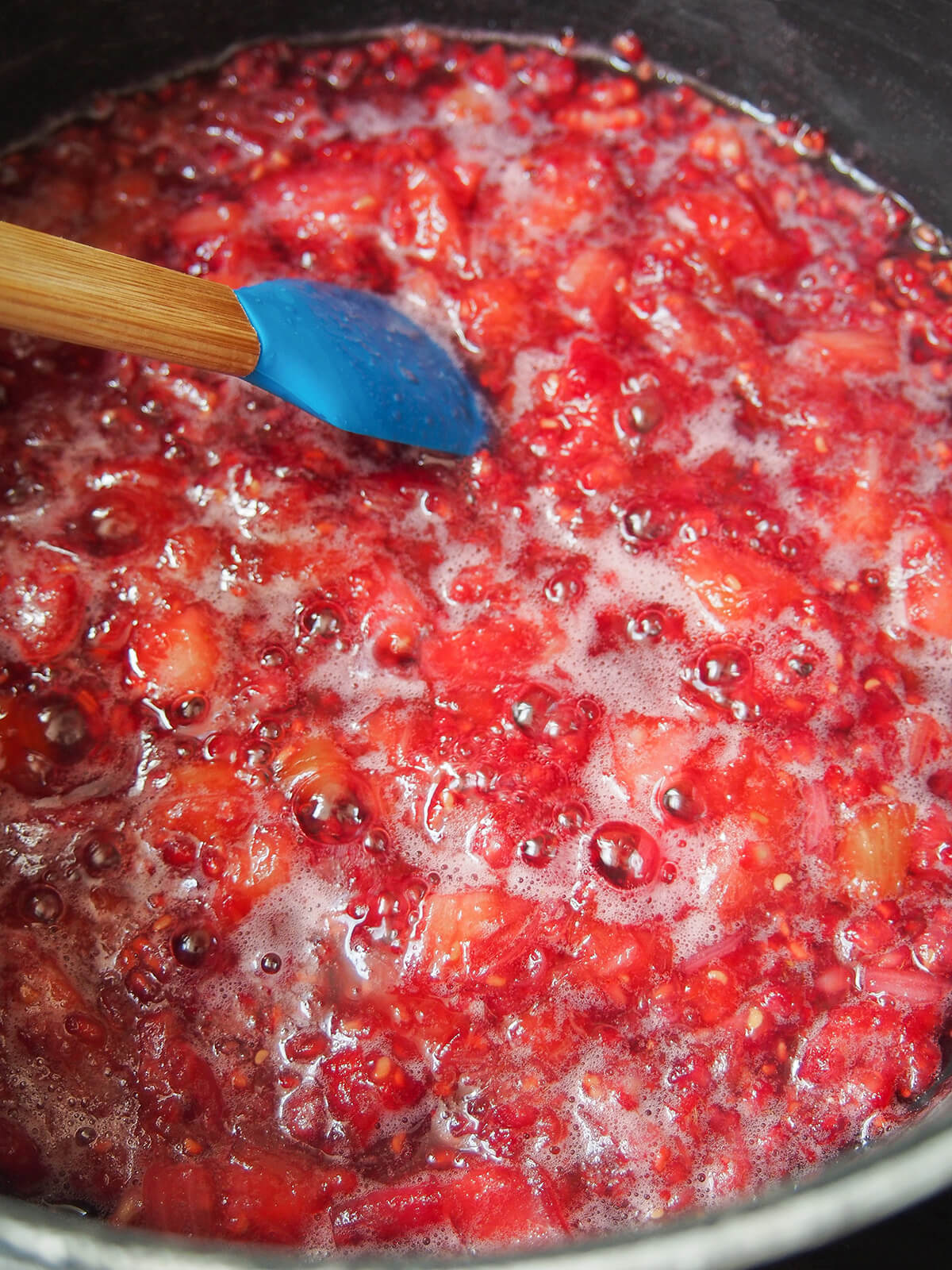 raspberry rhubarb jam simmering in pot with spatula to top of mixture.