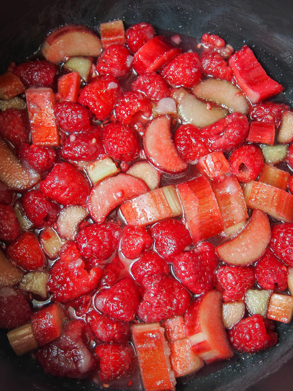 slices of rhubarb and raspberries with liquid around them as they soften in pan.