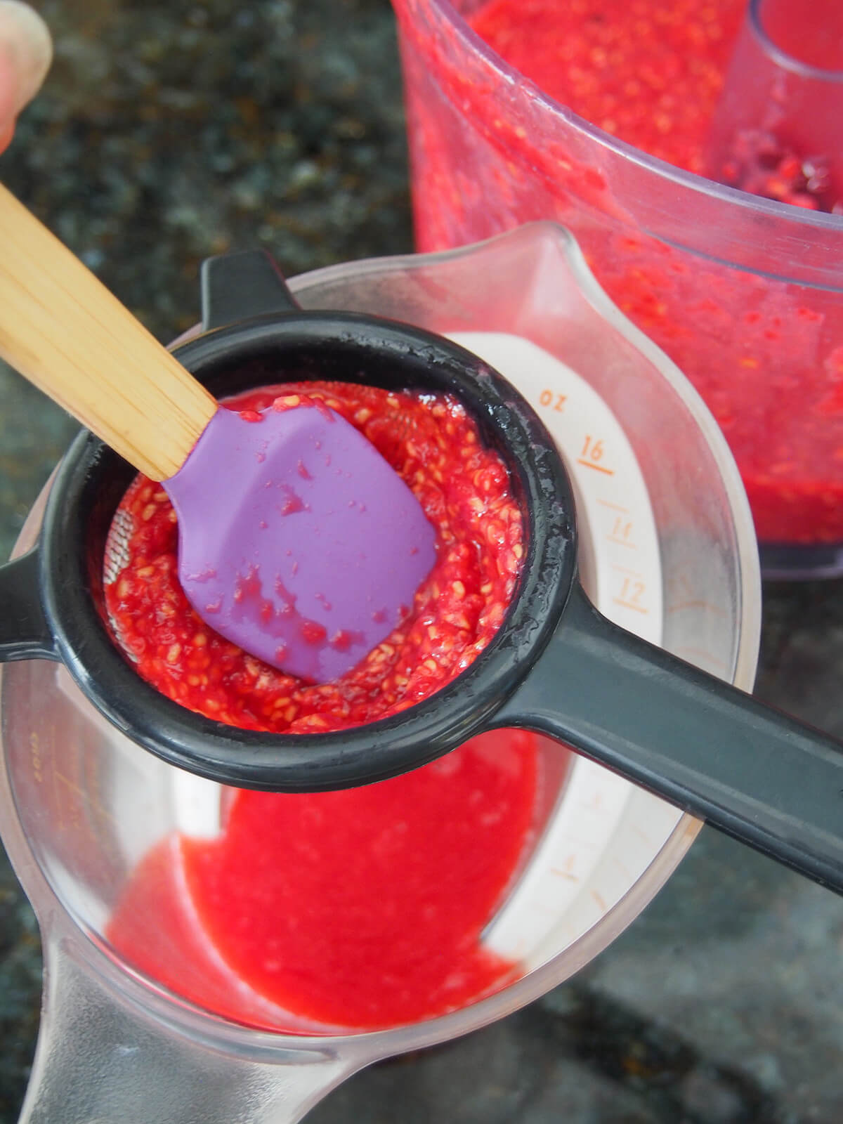 straining raspberry puree through a small strainer into a measuring jug.