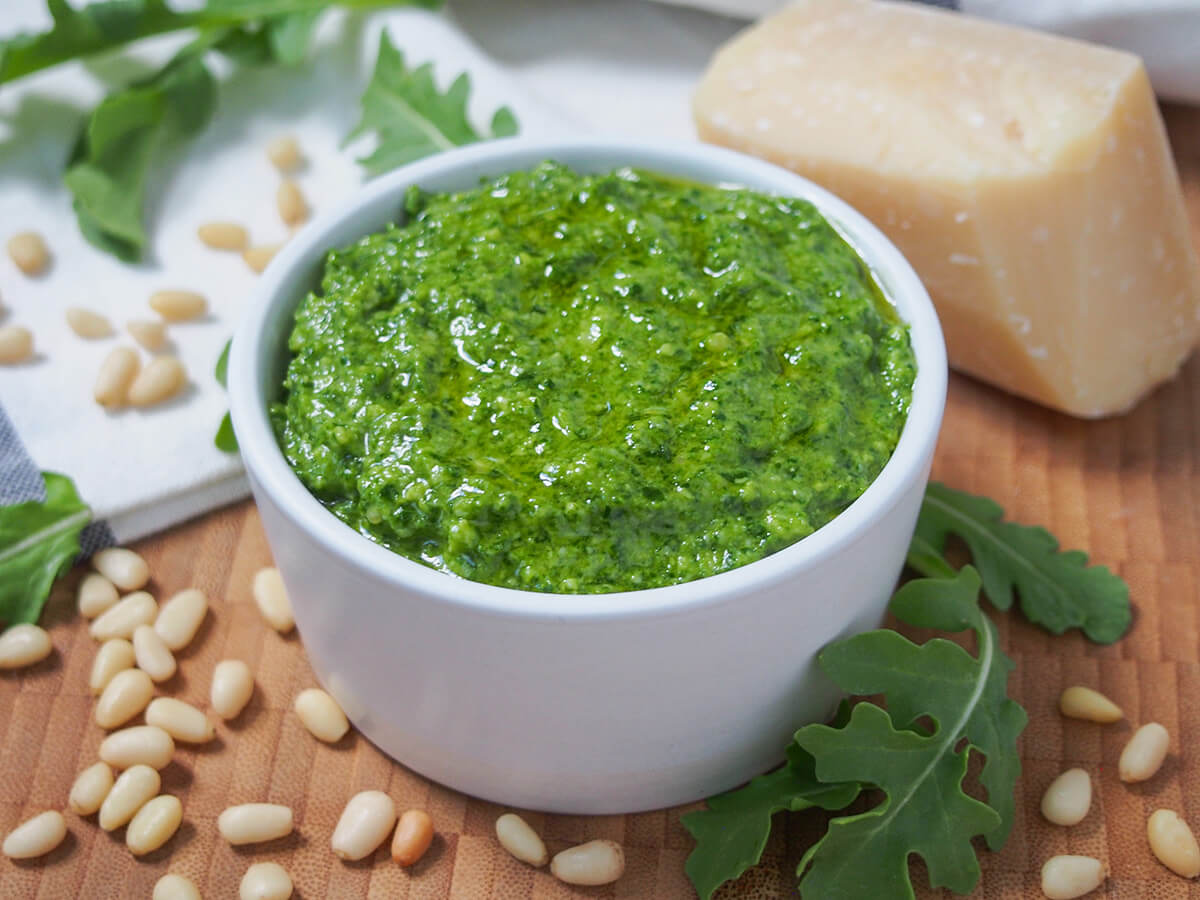 dish filled with arugula pesto with block of parmesan cheese behind.