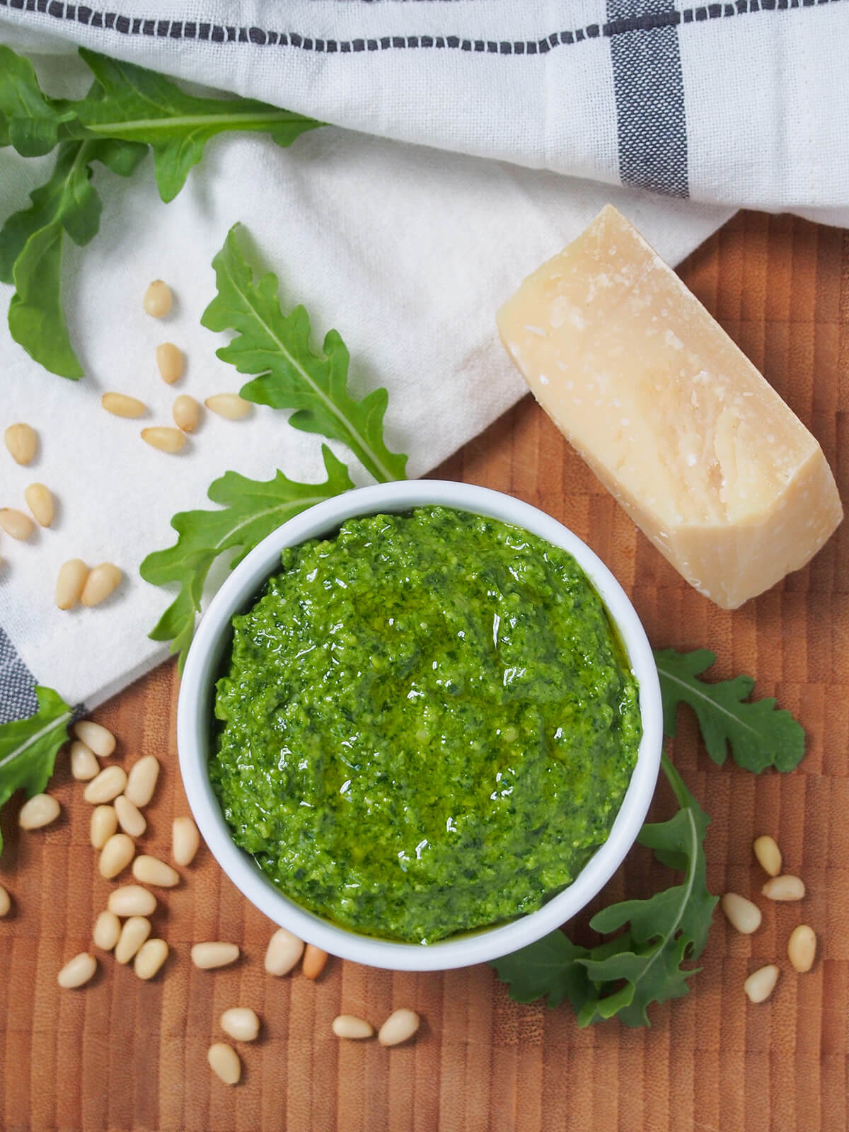 overhead view of dish of arugula pesto with leaves and pine nuts around.