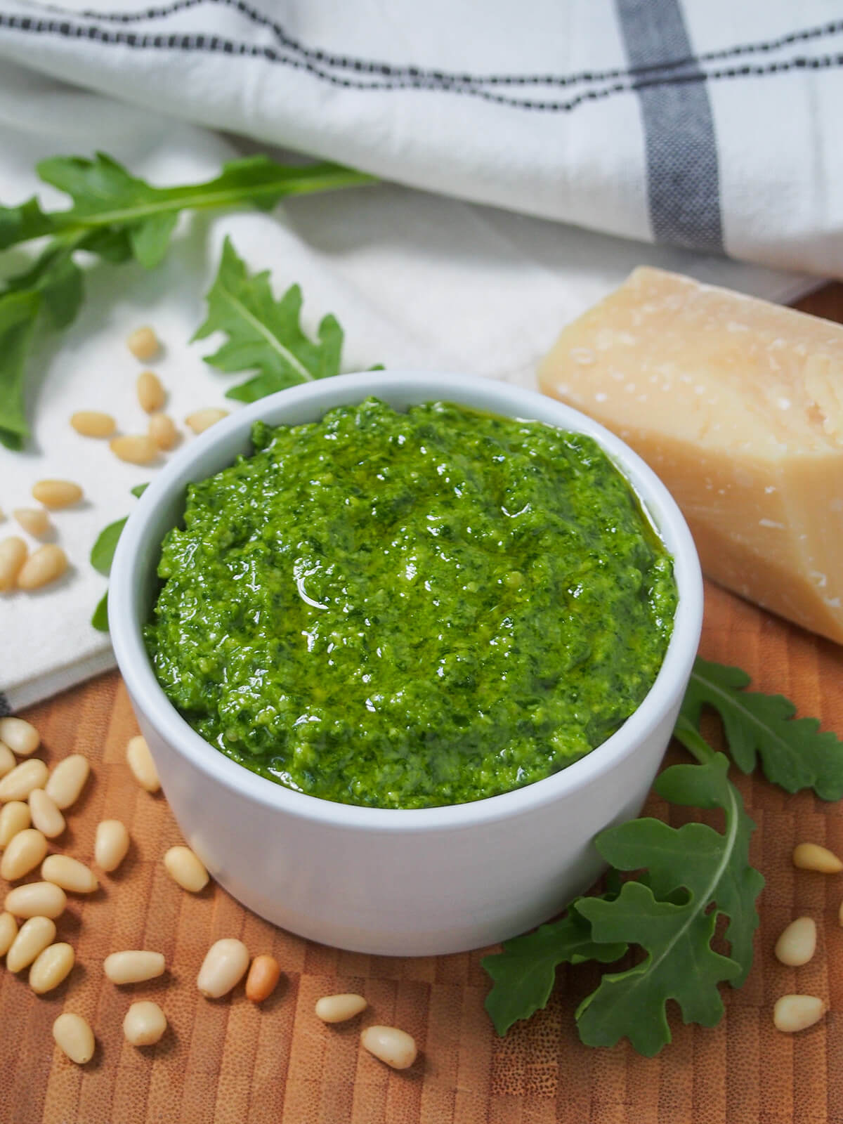 dish of arugula pesto with arugula leaves, cheese and pine nuts behind and to side.