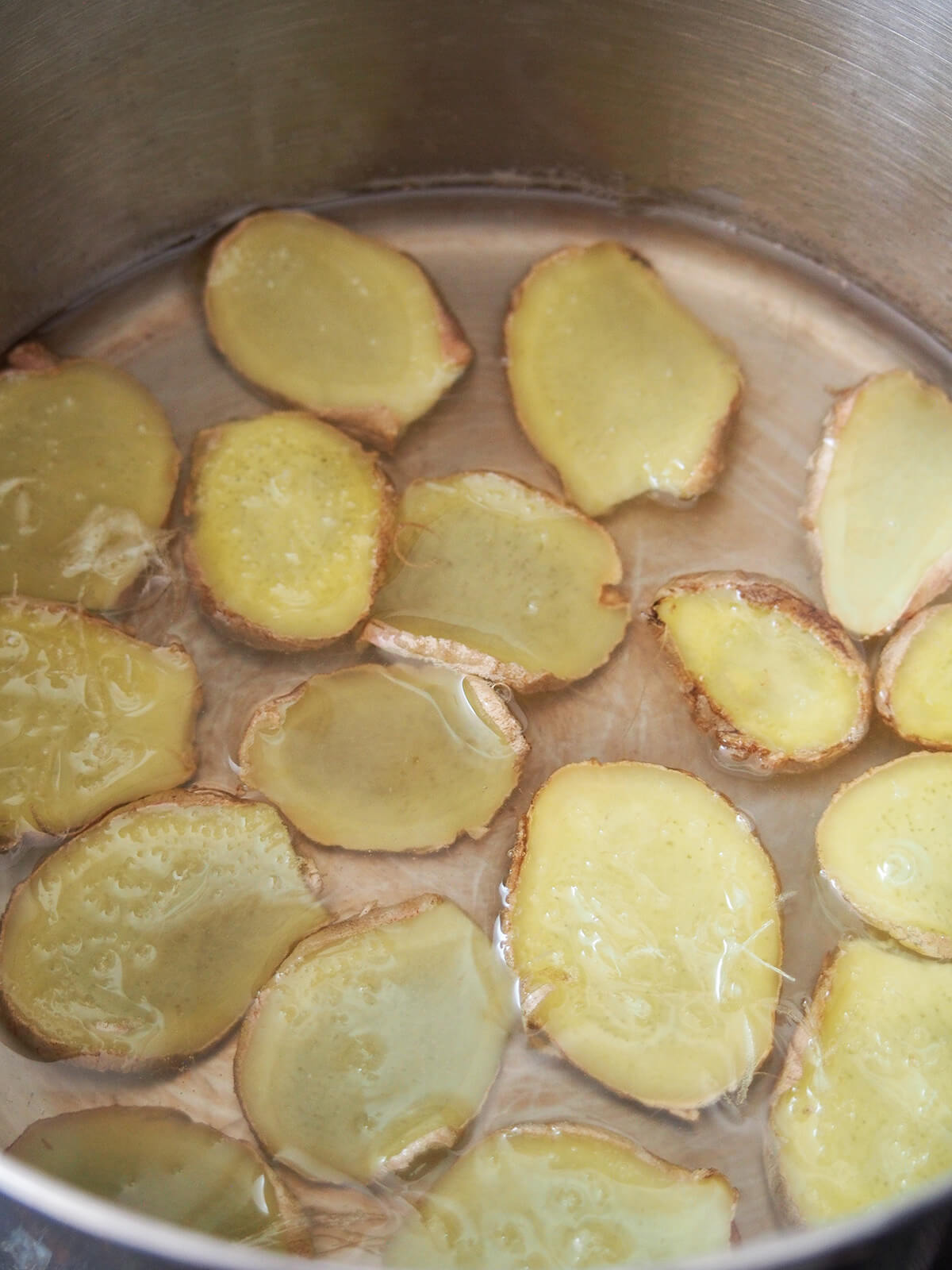 slices of fresh ginger sitting in syrup in a pan.