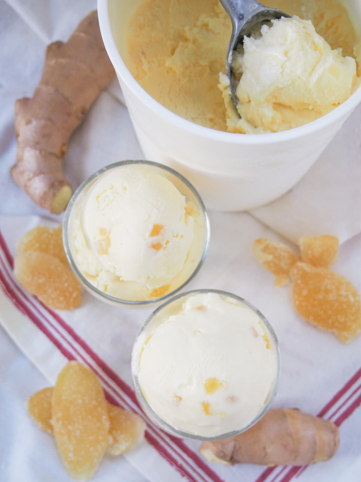overhead view of two glasses of ginger ice cream and scoop in tub with more, pieces of ginger and crystalized ginger around all.