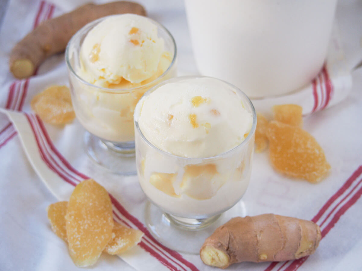 two glasses of ginger ice cream with fresh ginger and pieces of crystalized ginger either side.