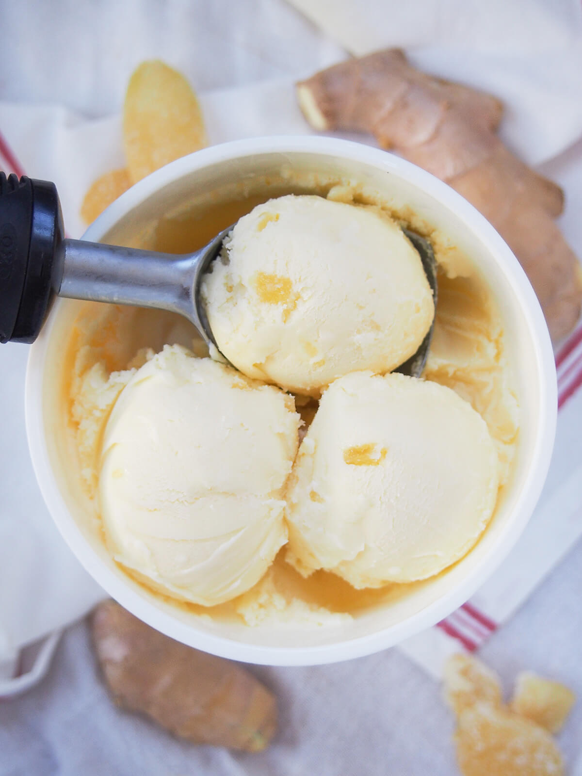 three scoops of ginger ice cream in tub from overhead with pieces of ginger in background below.
