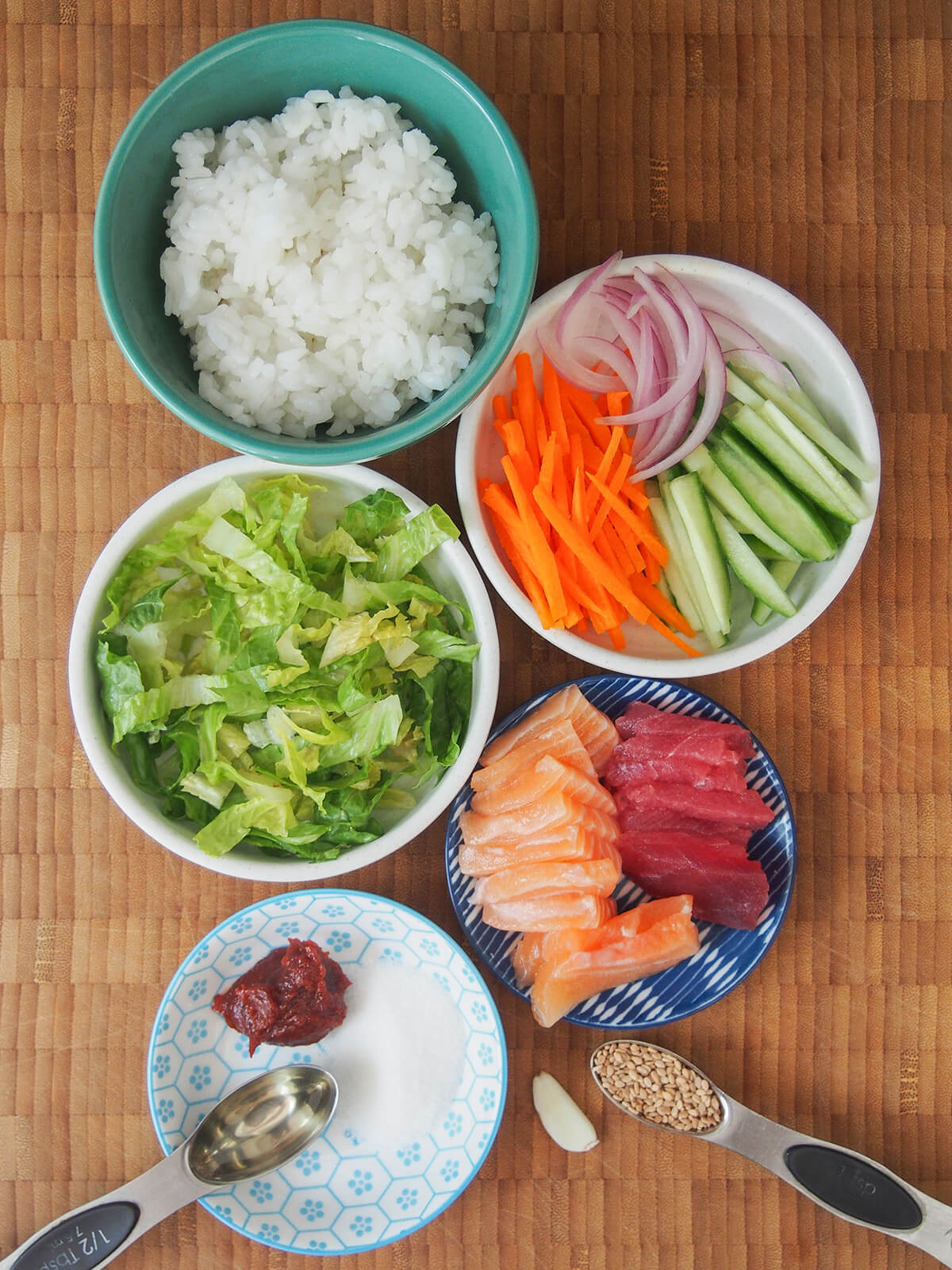 bowls with sliced raw fish, rice, vegetables in sticks and shredded lettuce.
