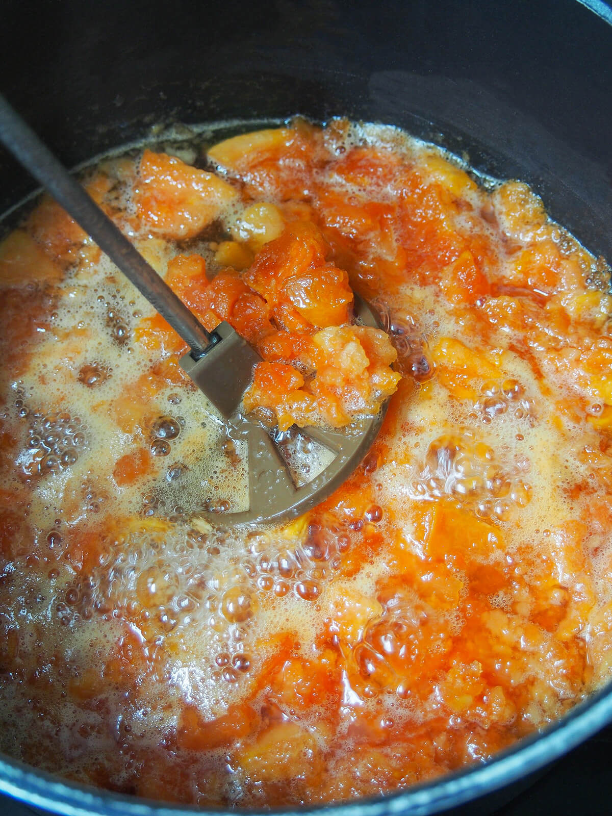 mashing papaya jam mashing pieces of papaya in syrupy liquid in pot to make jam.