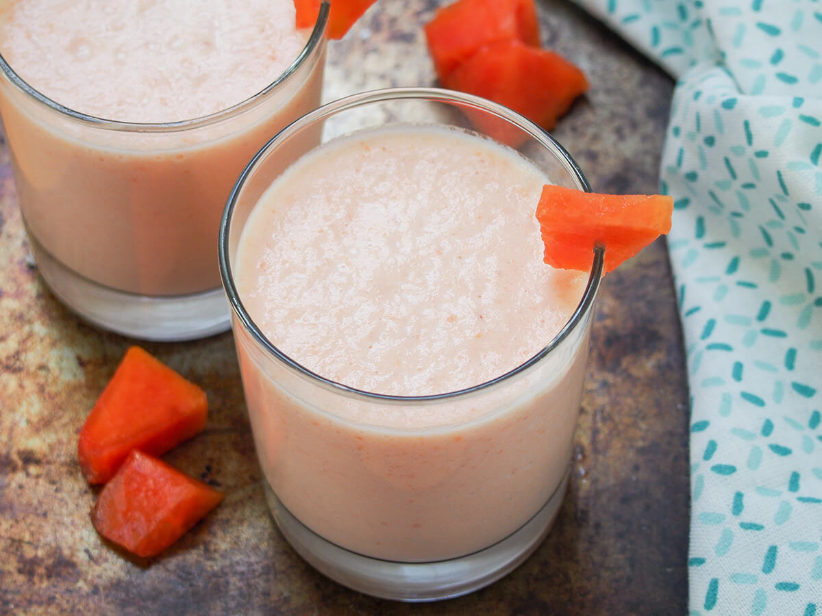 glass of papaya milkshake with pieces of papaya to side.