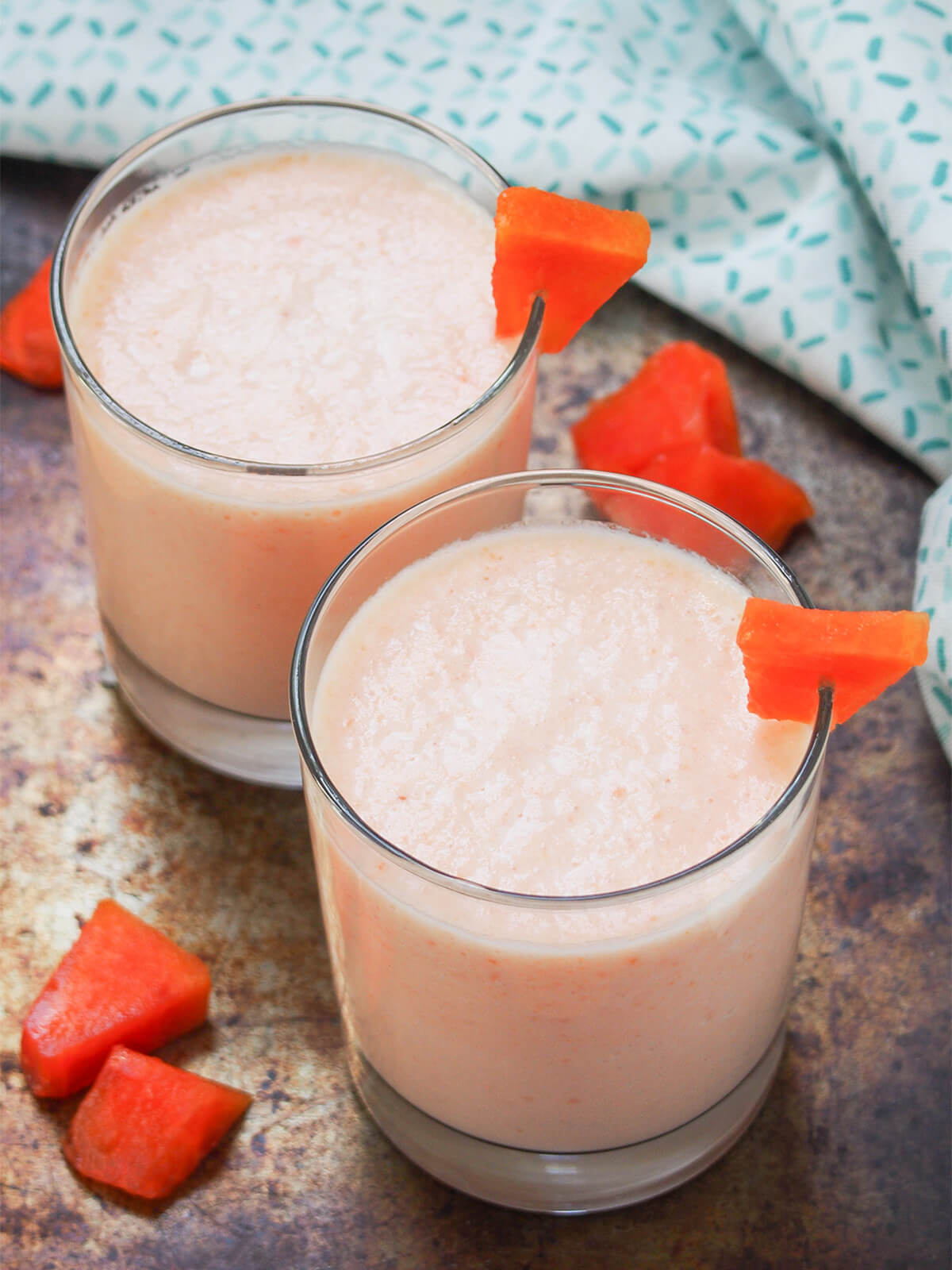 two glasses of papaya milkshake garnished with pieces of papaya and also papaya to side.