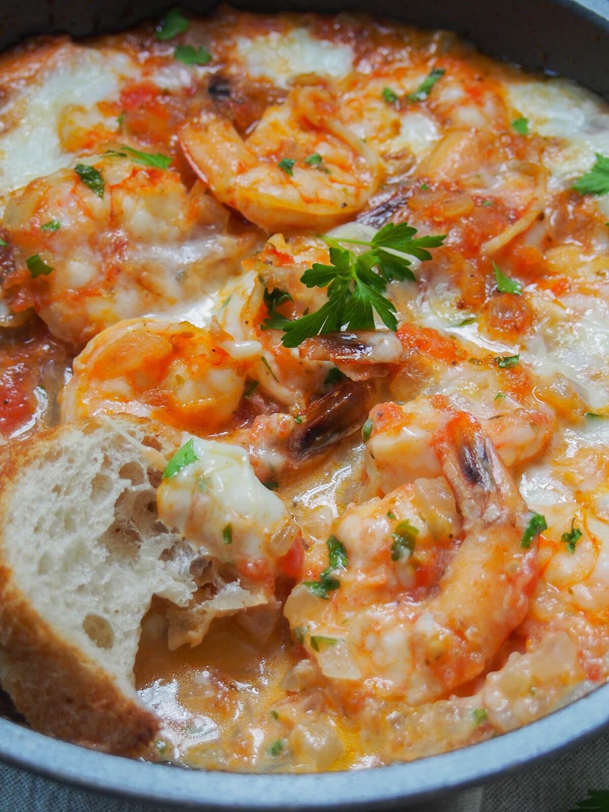 close up view of shrimp saganaki with a piece of bread in the sauce at front.