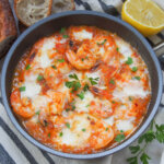 skillet of shrimp saganaki with lemon to side.