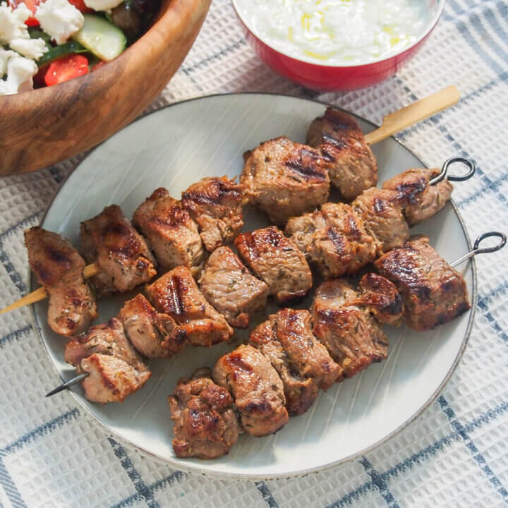 three Greek lamb souvlaki skewers on a plate.