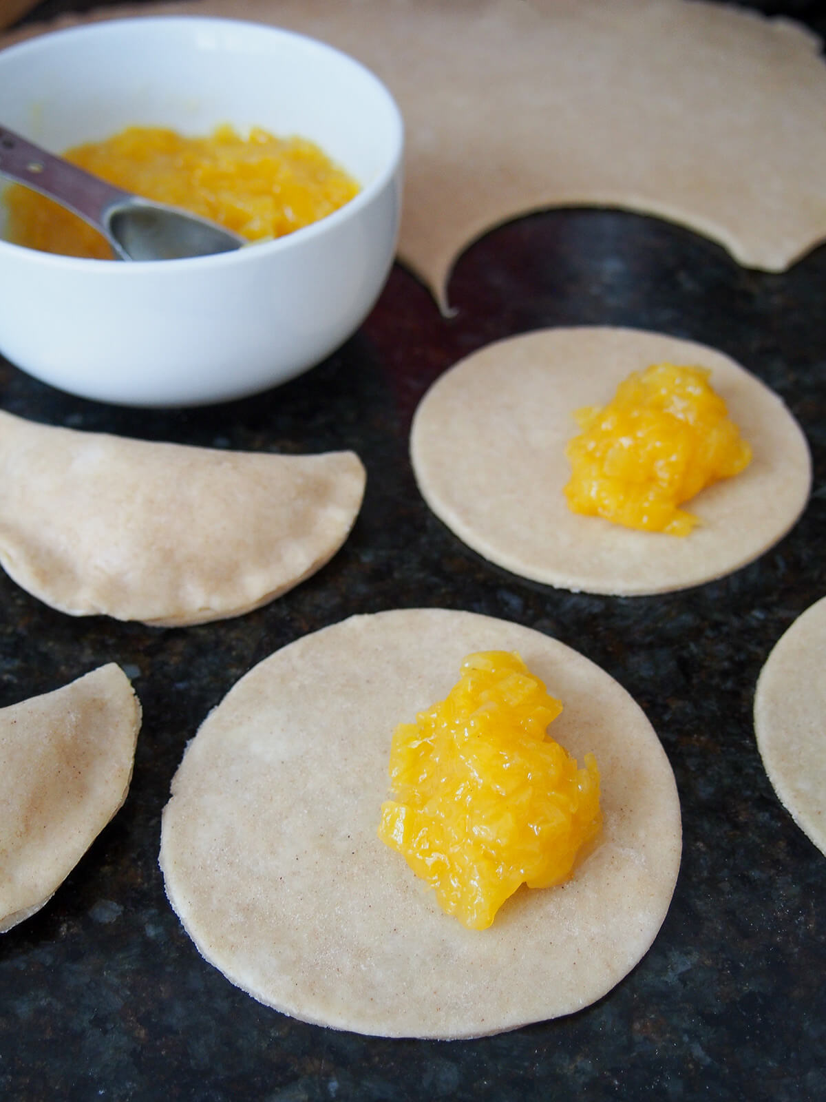 spoonfuls of pineapple filling sitting on rounds of pastry with more of both behind.