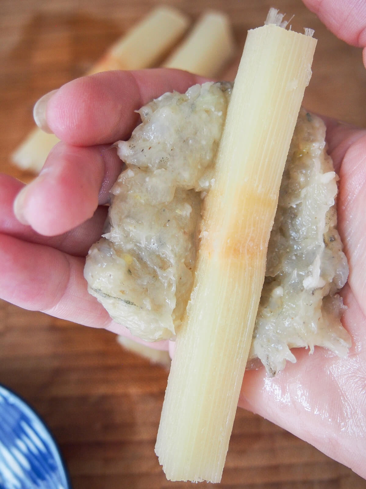 forming shrimp paste around stick of sugarcane with hand.