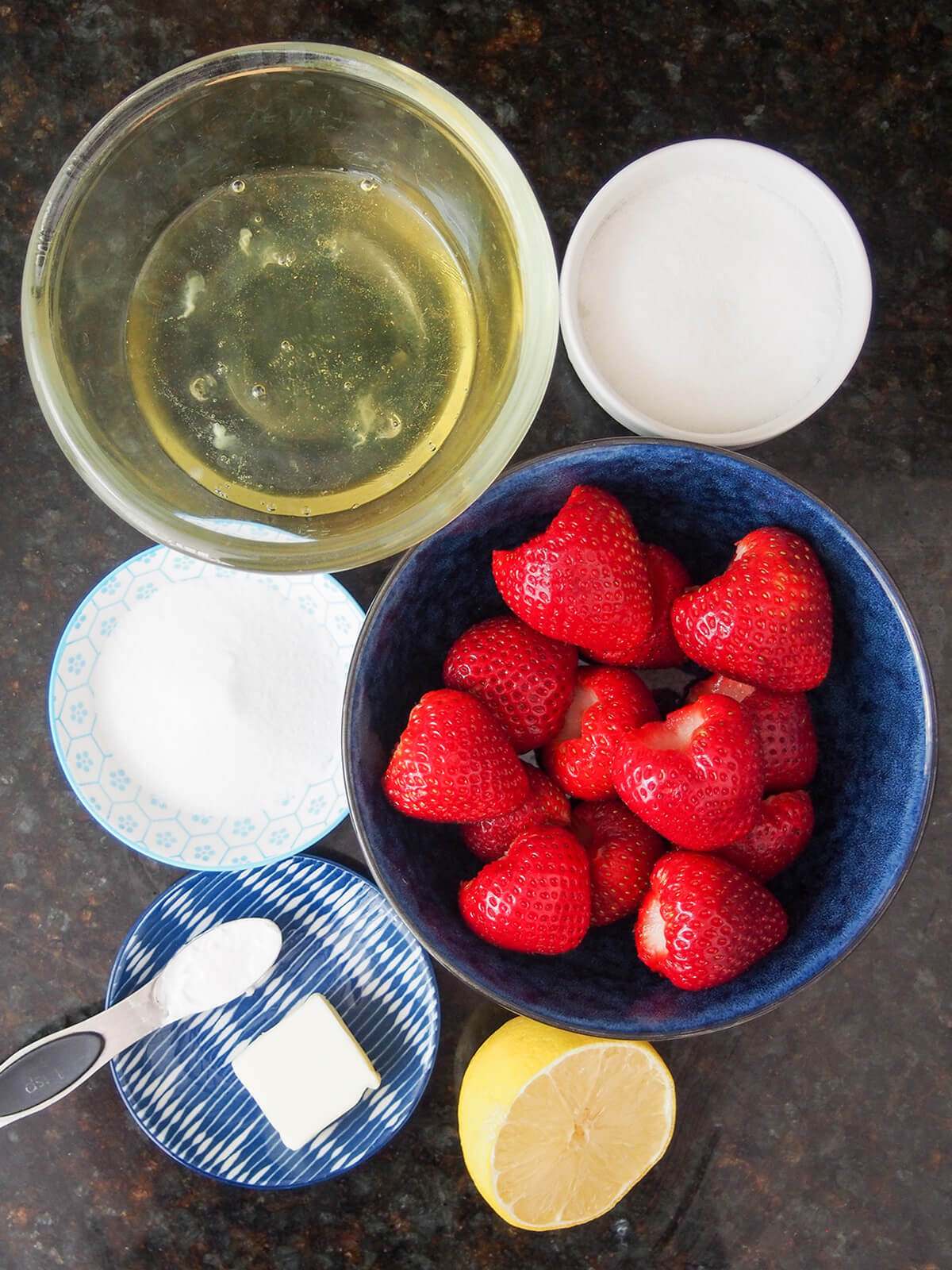 bowls of egg whites, strawberries and sugar with part lemon below and chunk butter.