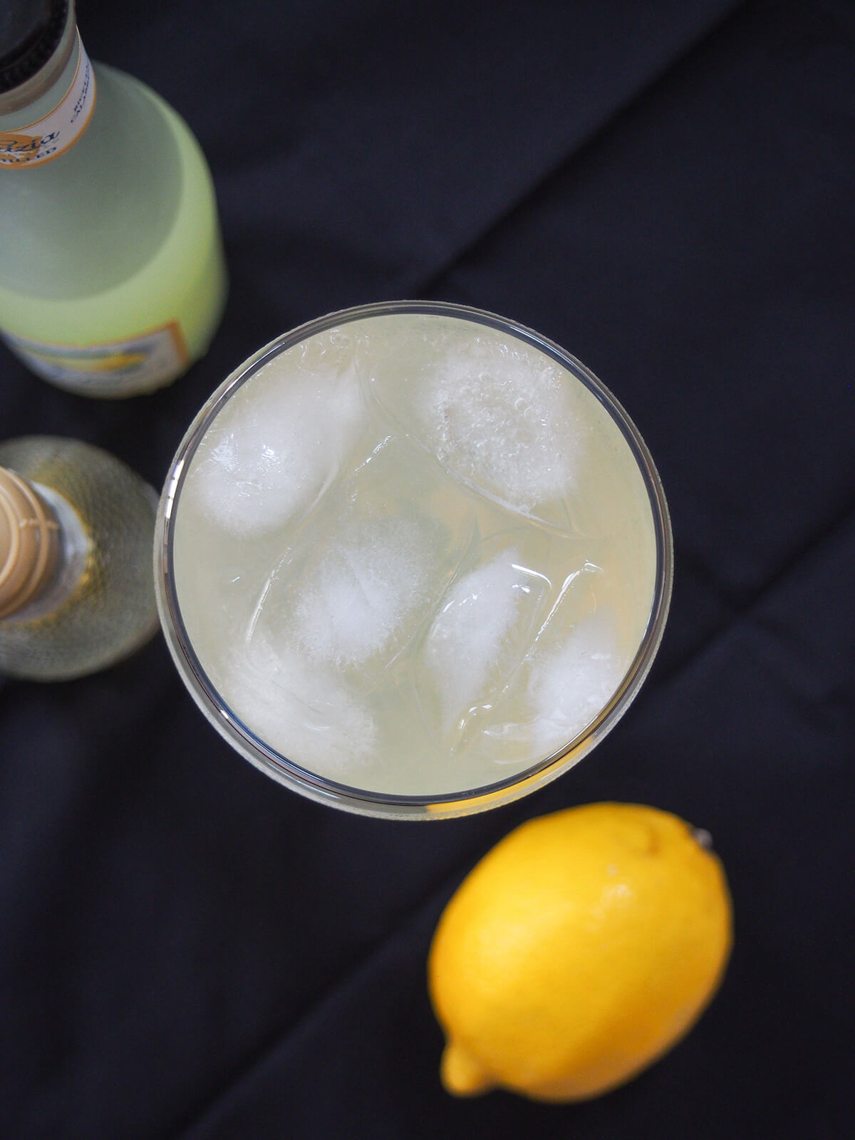 overhead view of a glass of limoncello spritz showing cubes of ice in drink with lemon below.