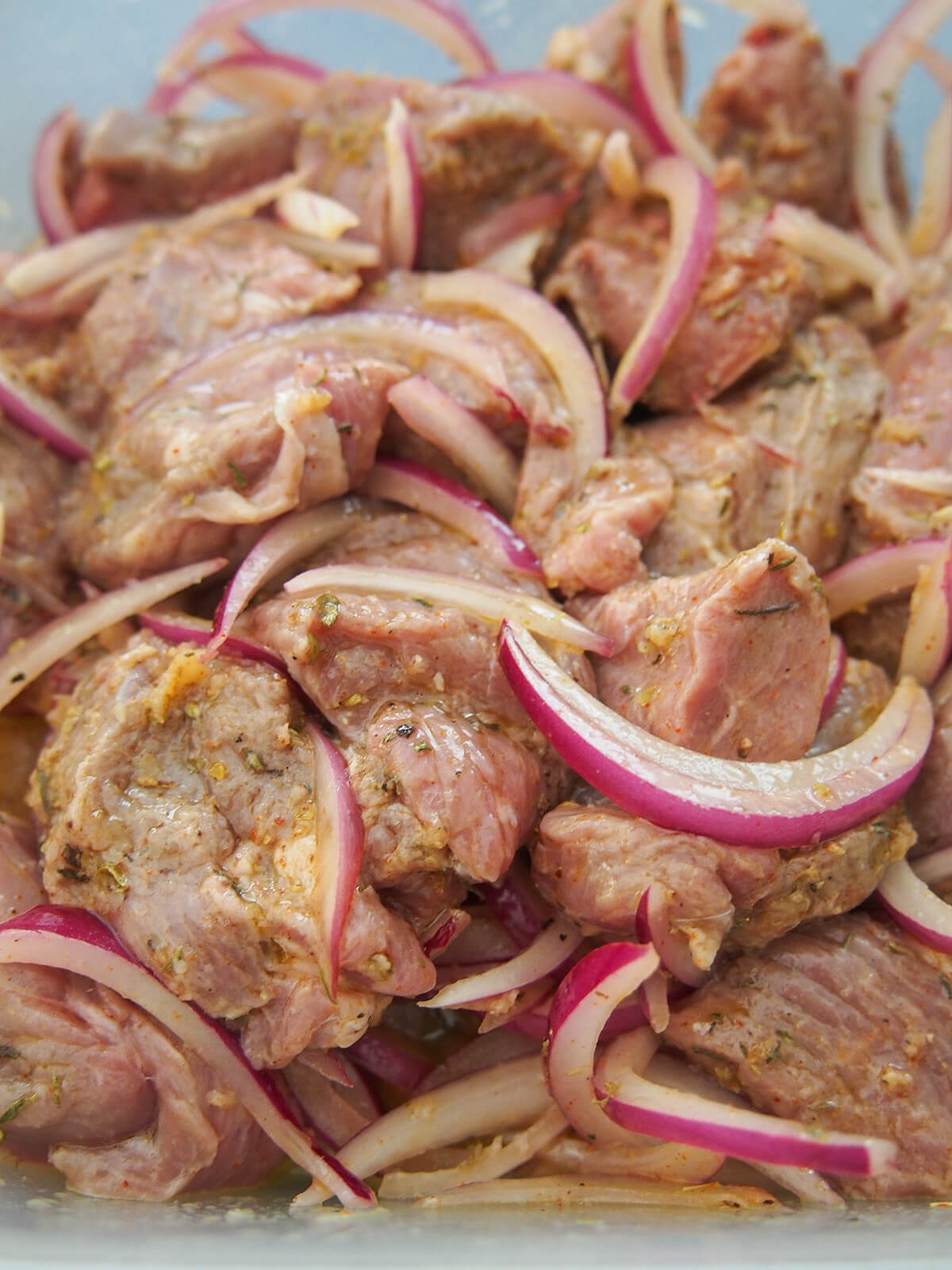 marinating lamb for Greek lamb souvlaki cubes of lamb in Greek style marinade with red onion slices and herbs visible.