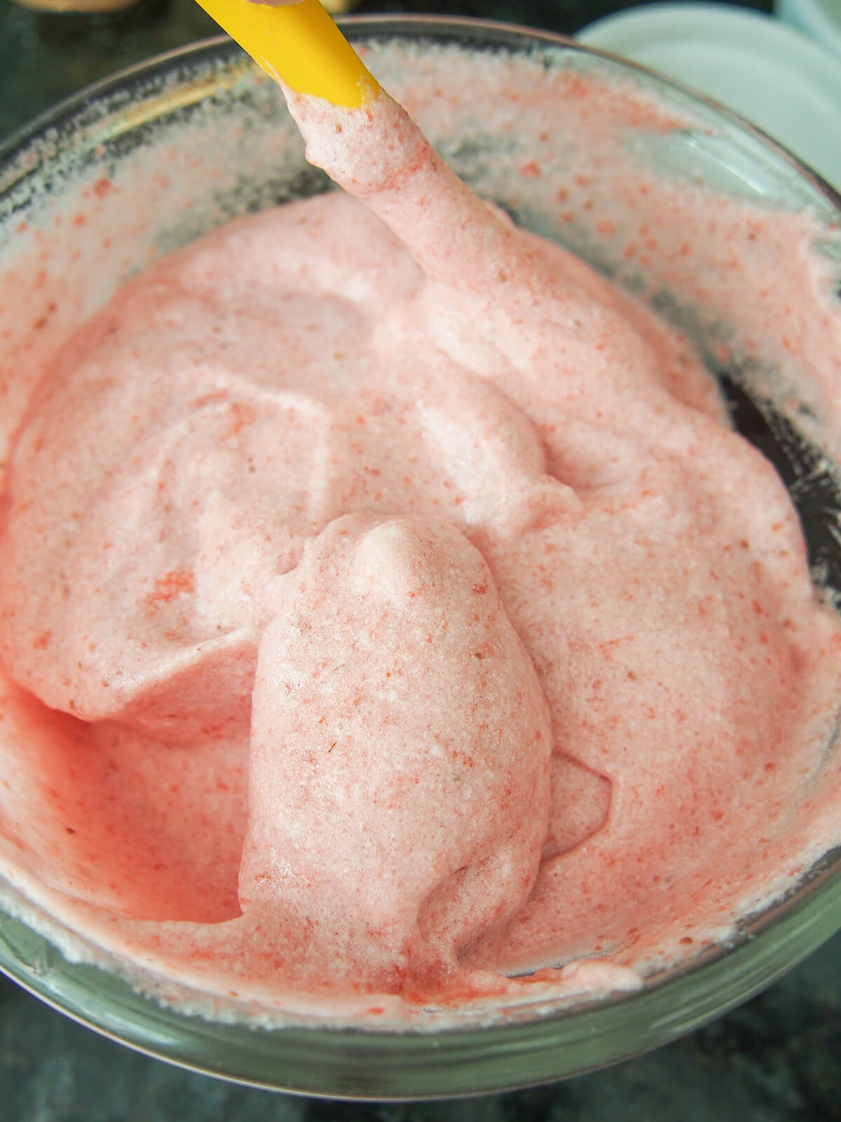 strawberry egg white mixture in bowl with spatula at back.