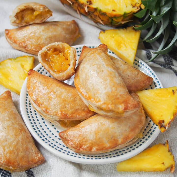 plate of pineapple empanadas with chunks of pineapple around them and one empanada broken open showing filling.