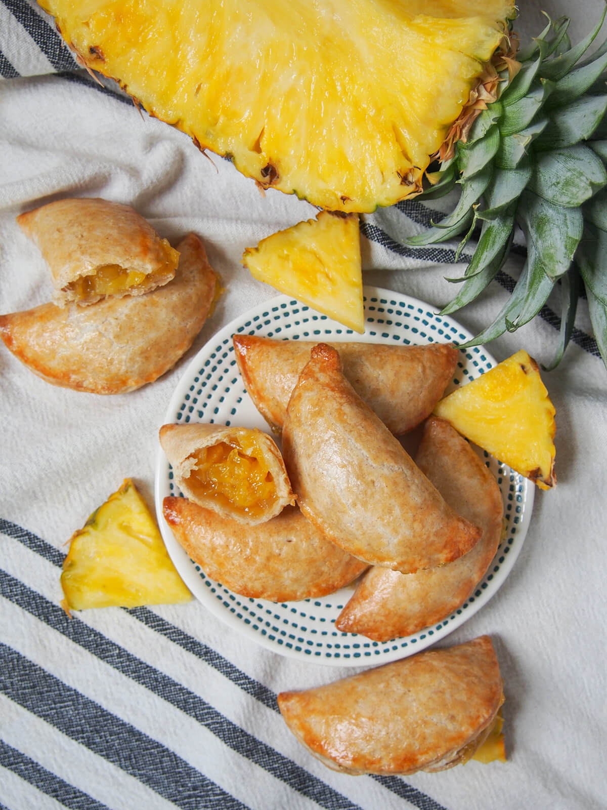 overhead view of a plate of pineapple empanadas with some to wither side of plate and part pineapple at top.