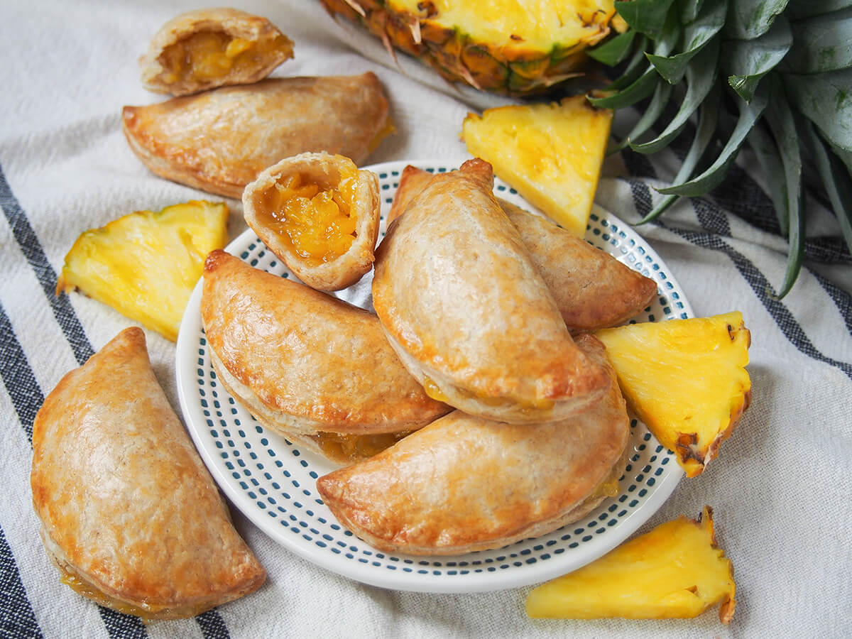 plate of pineapple empanadas with one broken open showing filling and pieces of pineapple around.