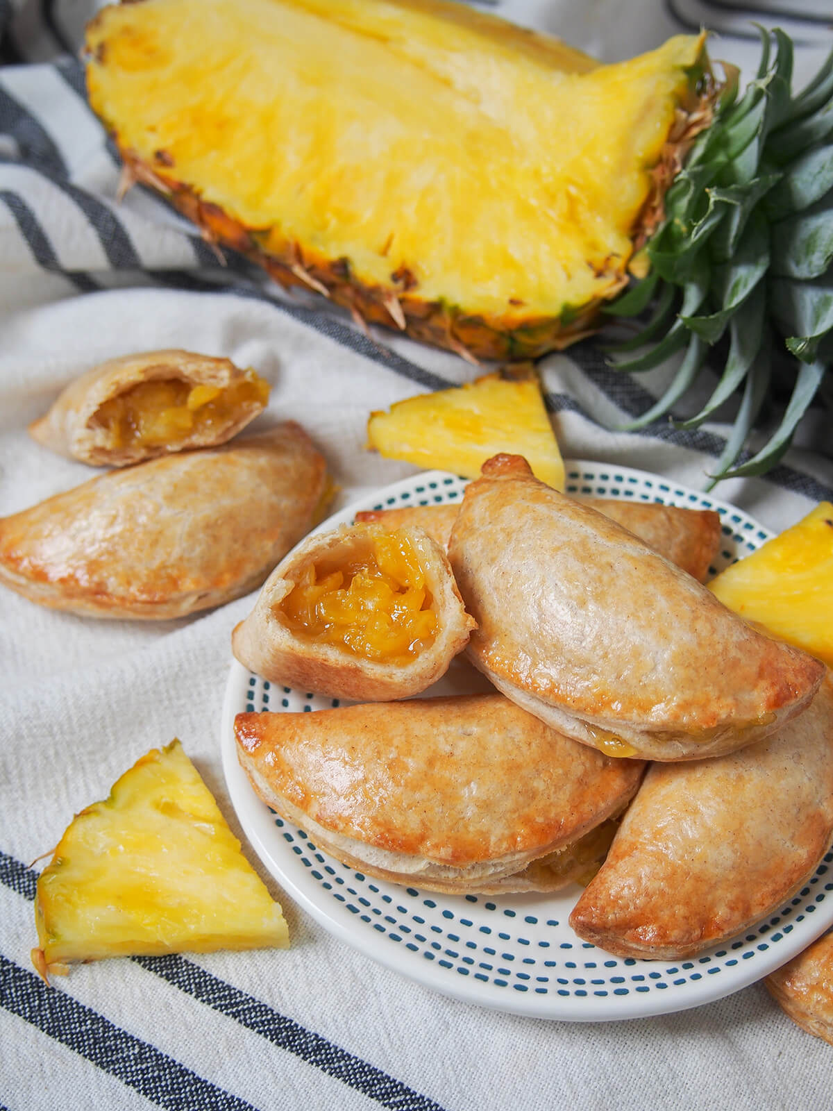 plate of pineapple empanadas with part pineapple behind and pieces of pineapple around and other empanada to side.