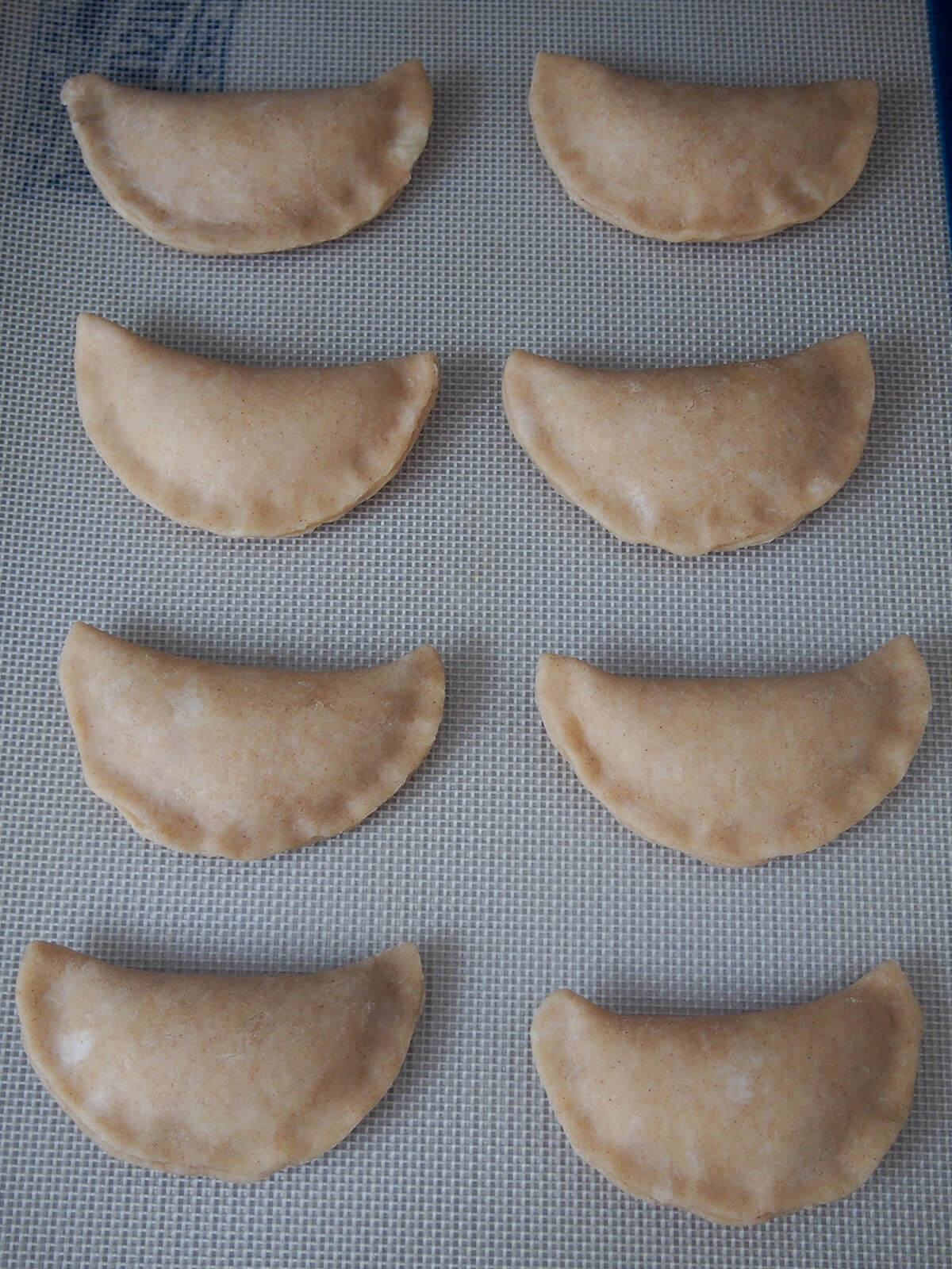 uncooked pineapple empanadas on lined baking sheet.
