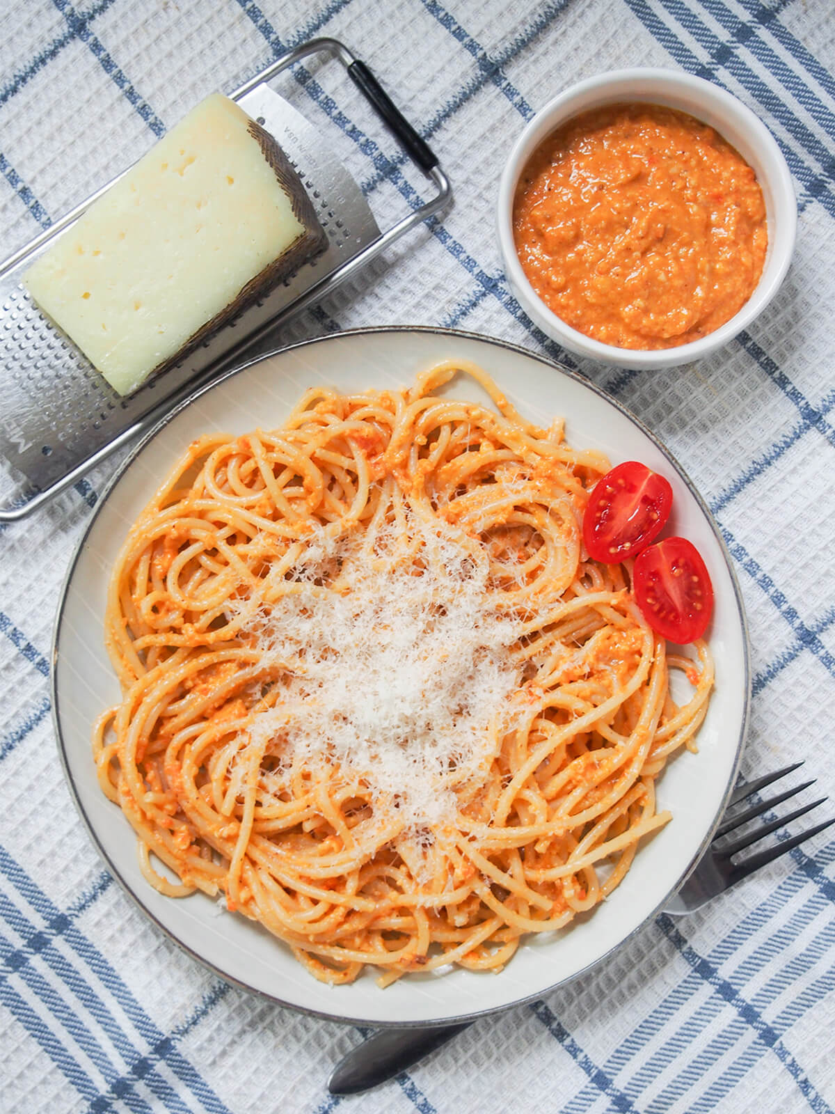 overhead view of plate of romesco pasta with cheese and dish of romesco sauce above.