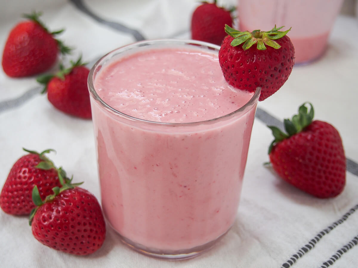 glass of strawberry lassi. side view of a glass of strawberry lassi with strawberries either side.