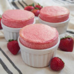 three ramekins of strawberry souffle with strawberries around them.