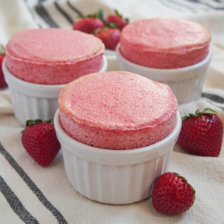 three ramekins of strawberry souffle with strawberries around them.