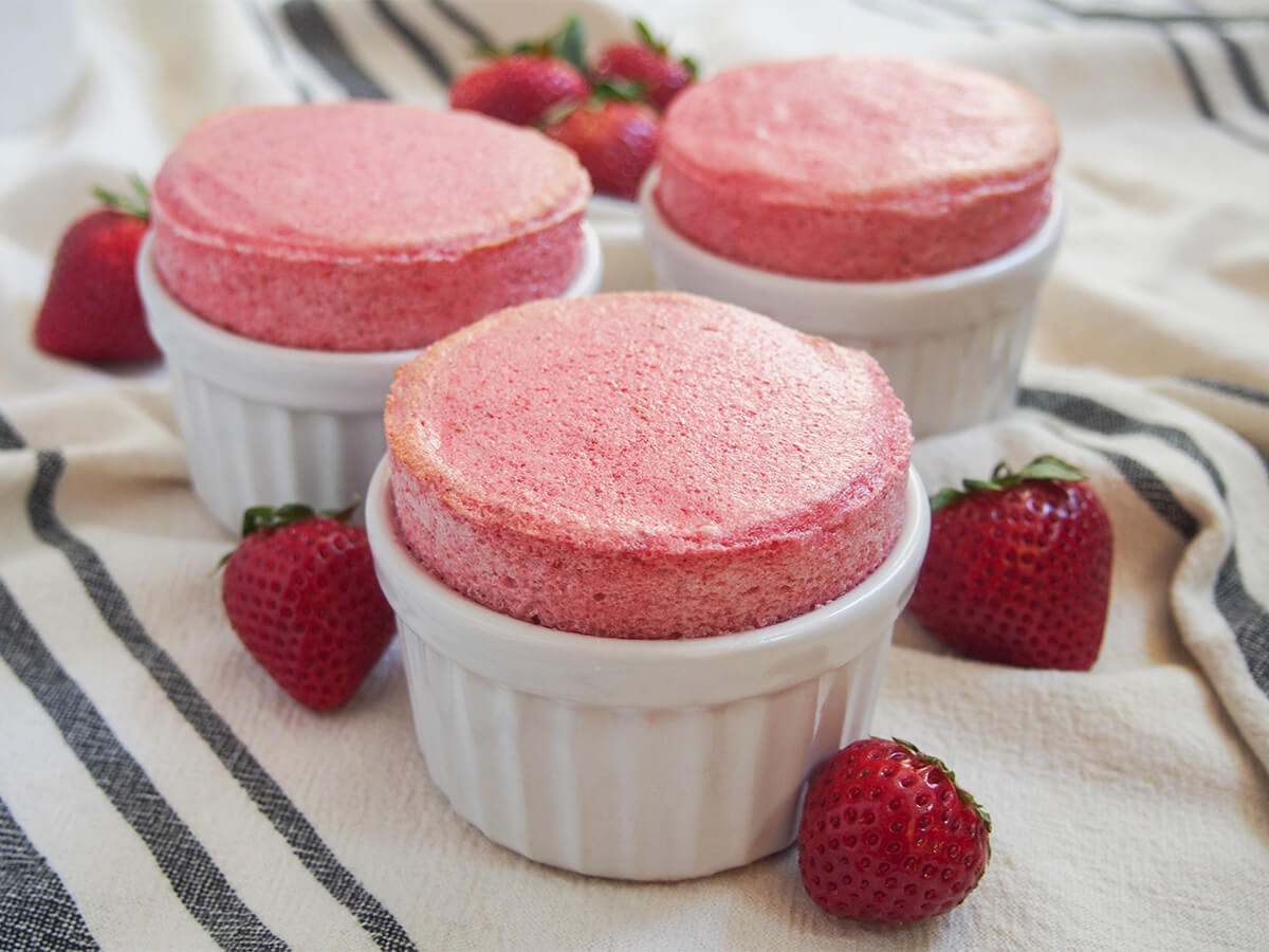three ramekins of strawberry souffle with strawberries around them.