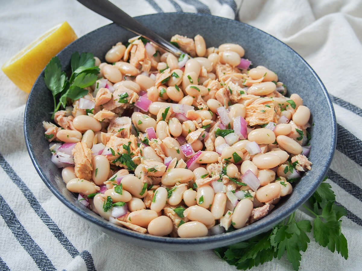 bowl of Tuscan white bean and tuna salad bowl of Tuscan white bean and tuna salad with lemon behind bowl and parsley in front.