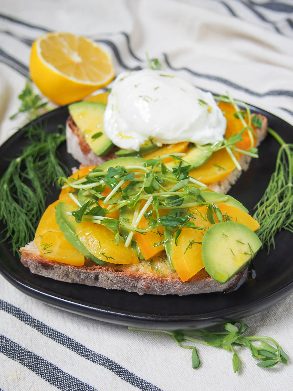 slices of avocado tartine with golden beet on plate with lemon behind.