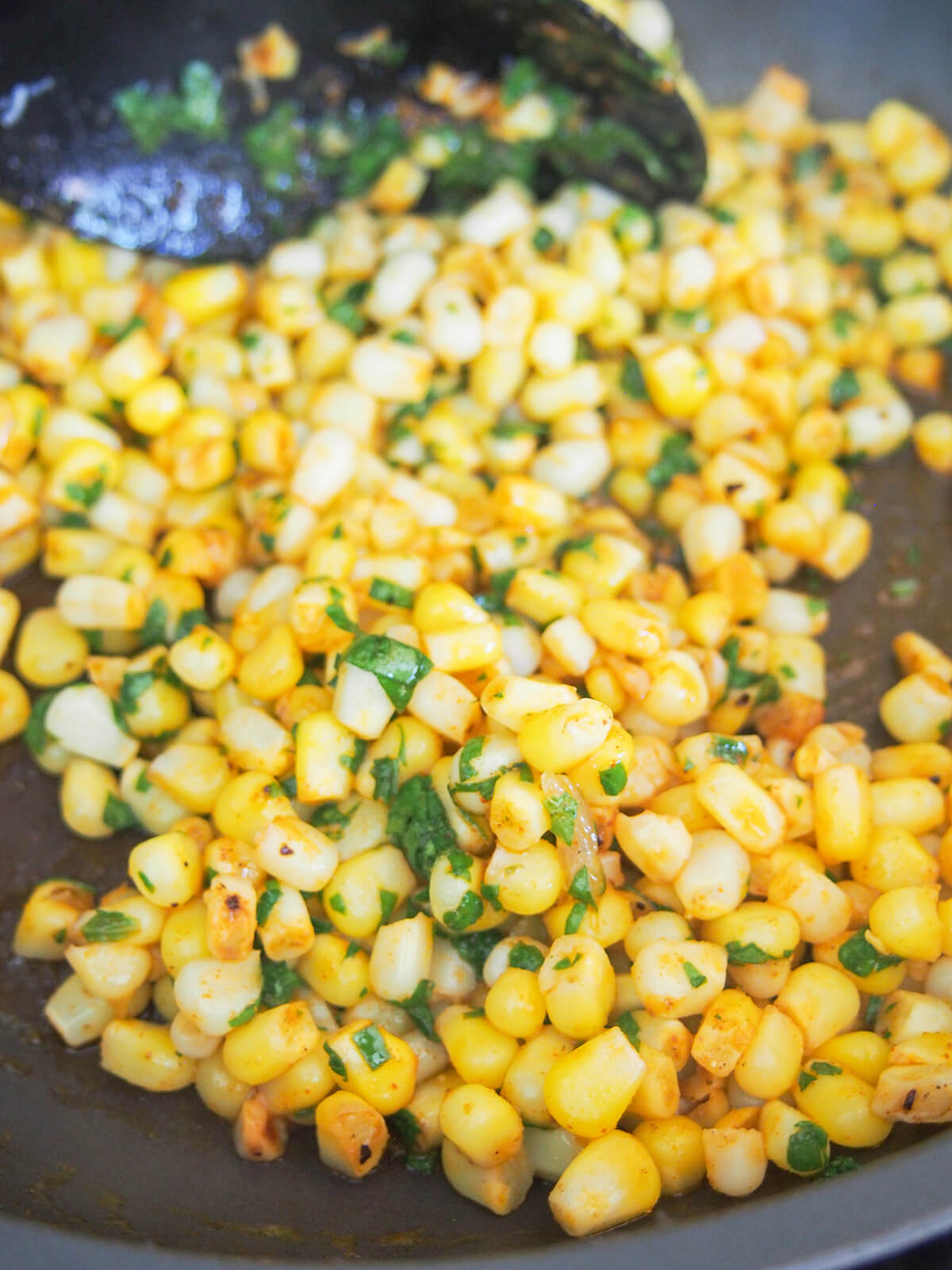 corn in skillet with herbs added and spoon to back.