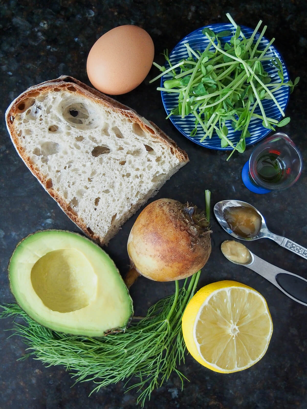 slices of bread, half avocado, lemon, golden beet, egg and small plate with pea shoots.