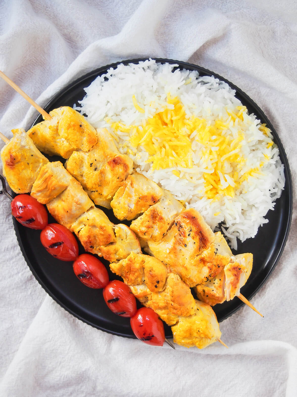 plate with rice, two jujeh kabab and skewer of grilled tomatoes from overhead.